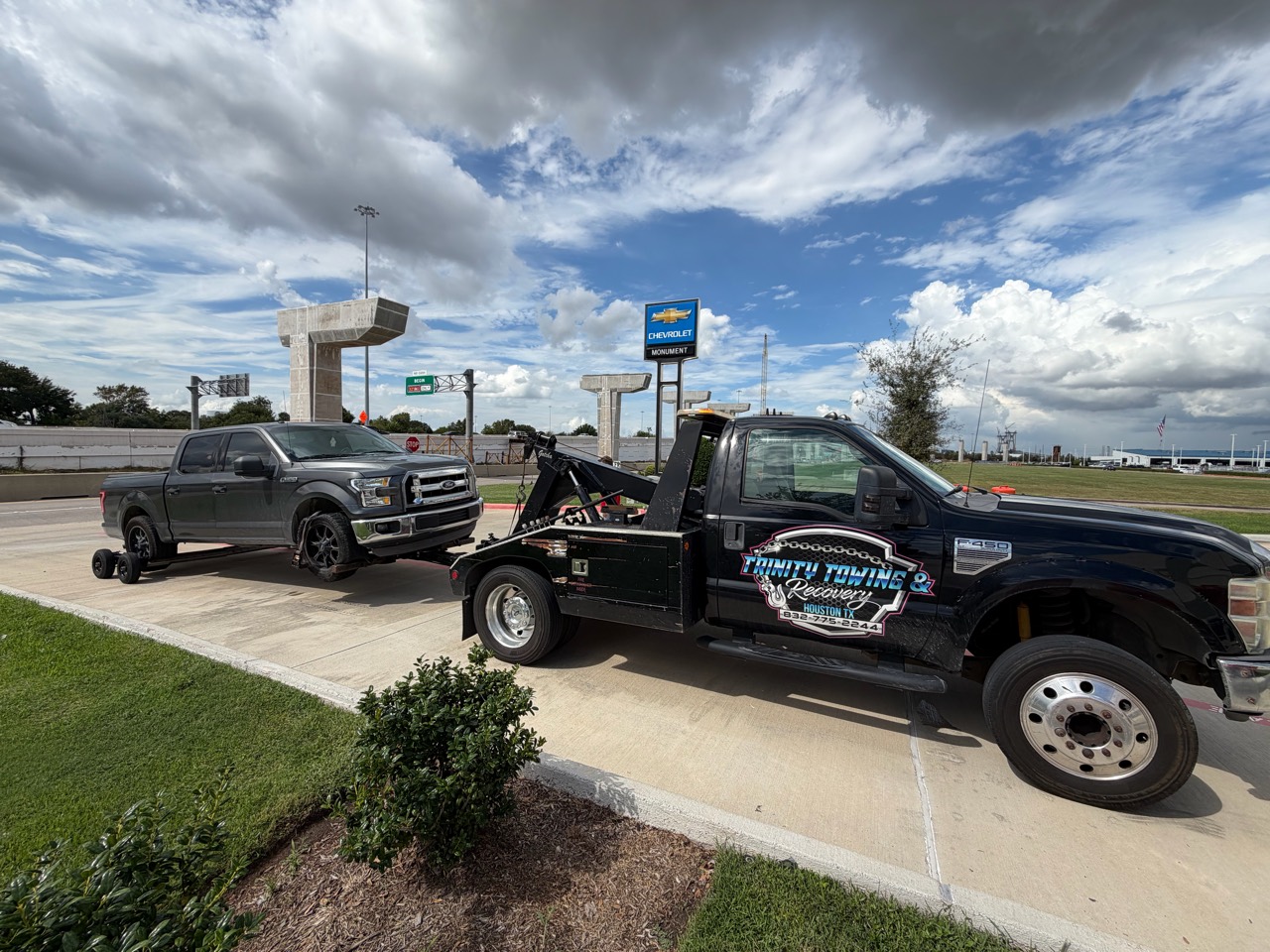 Trinity wheel-lift tow truck transporting a gray Ford F-150 with rear dollies