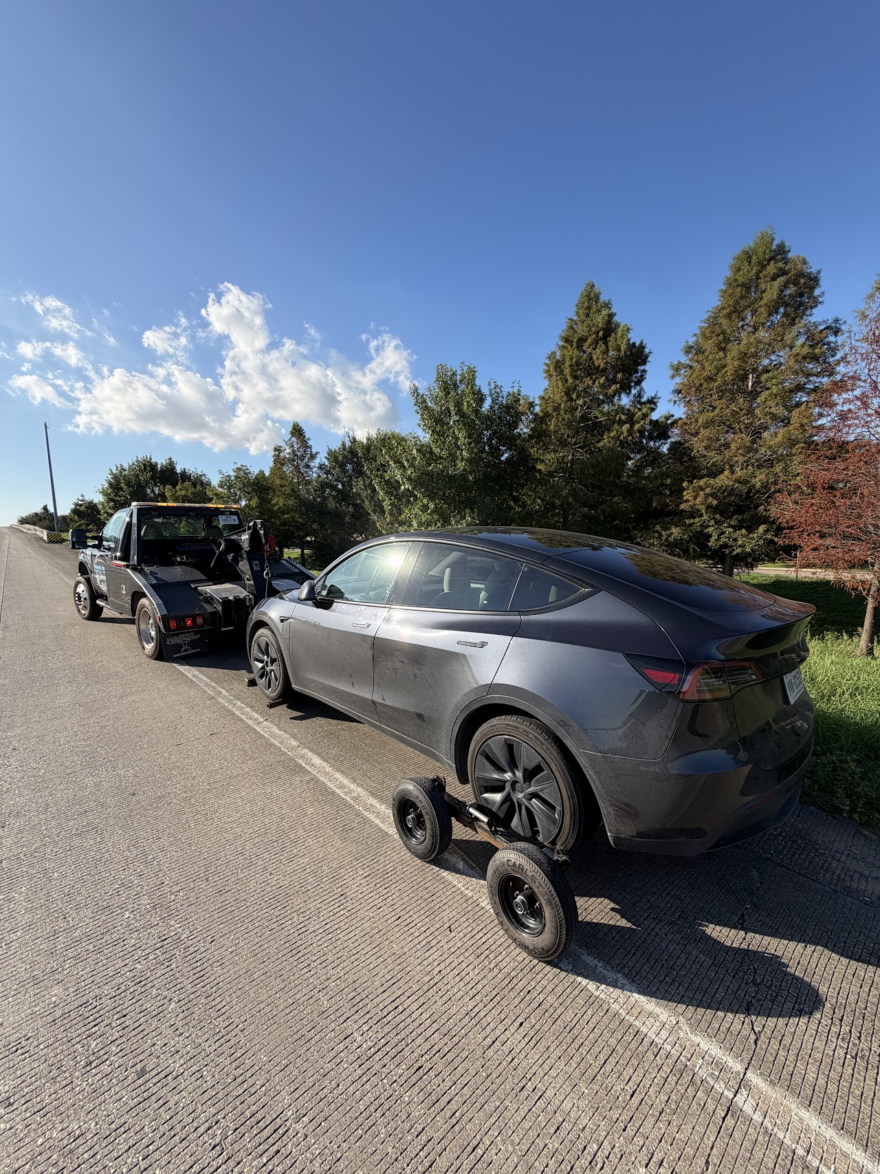 Gray Tesla supported by a wheel-lift and rear towing dollies
