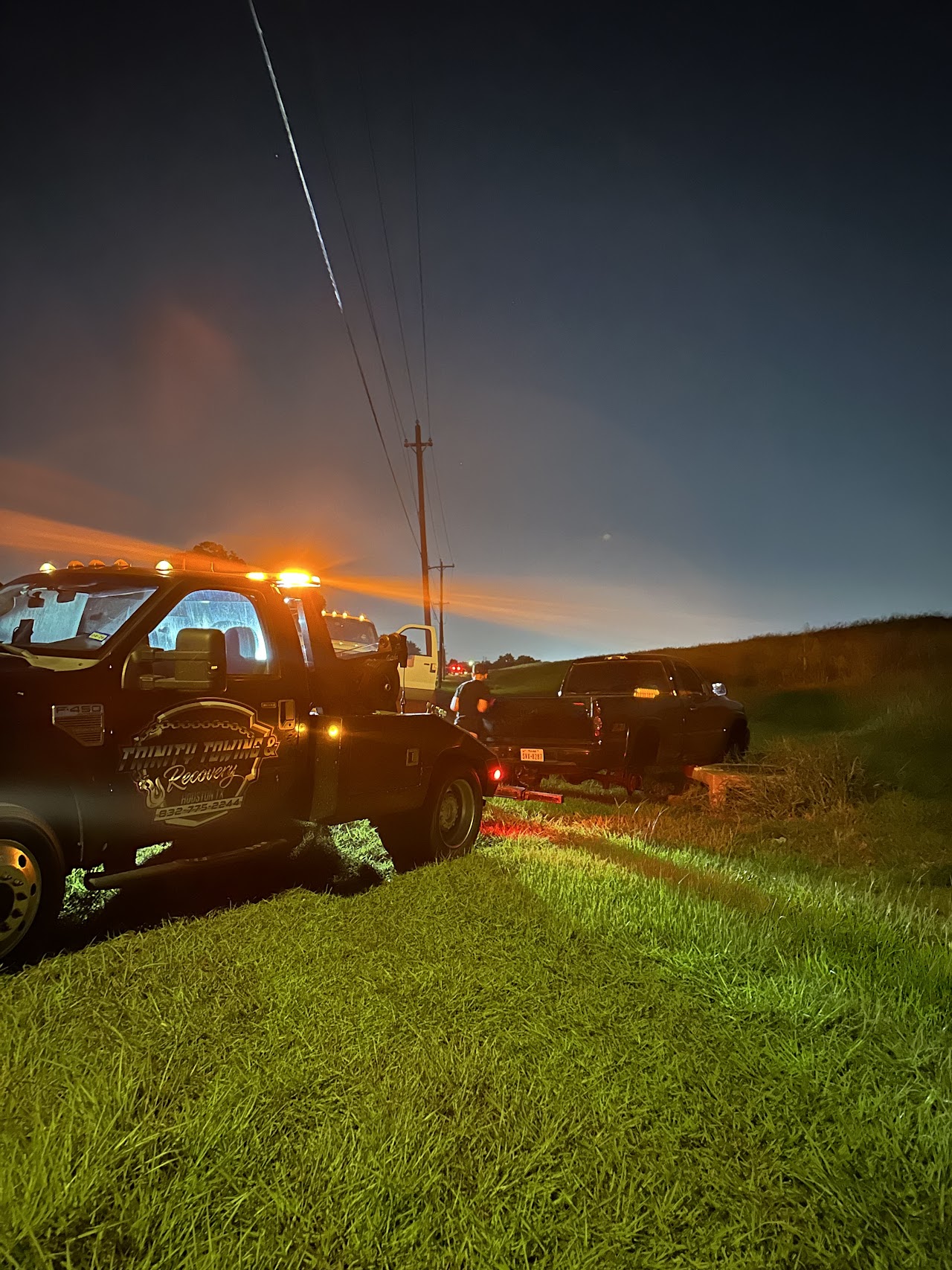 Our tow truck alongside a pickup on grass after dark