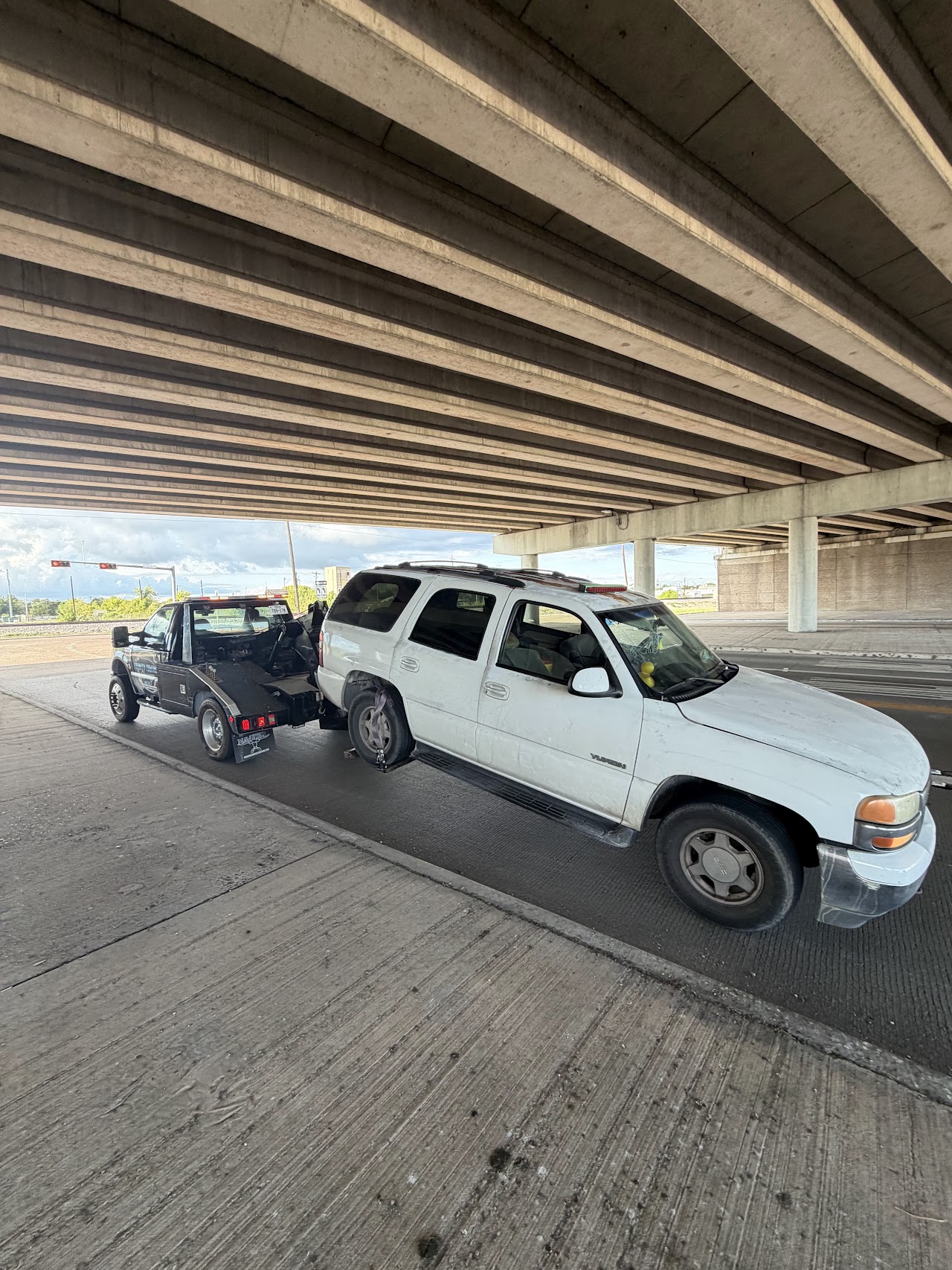 White SUV with its rear wheels lifted by our tow truck beneath SH-225 at Tidal Road
